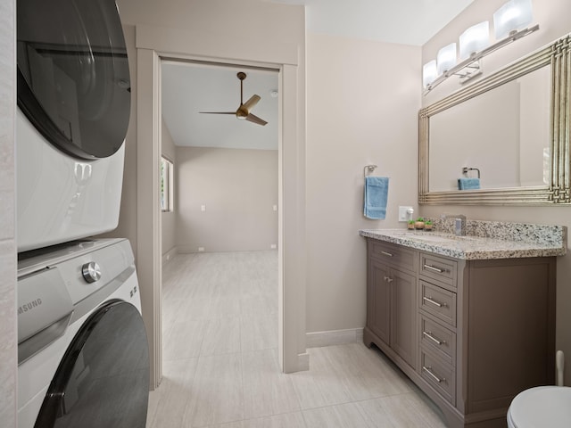 bathroom with stacked washer / dryer, a ceiling fan, vanity, baseboards, and toilet
