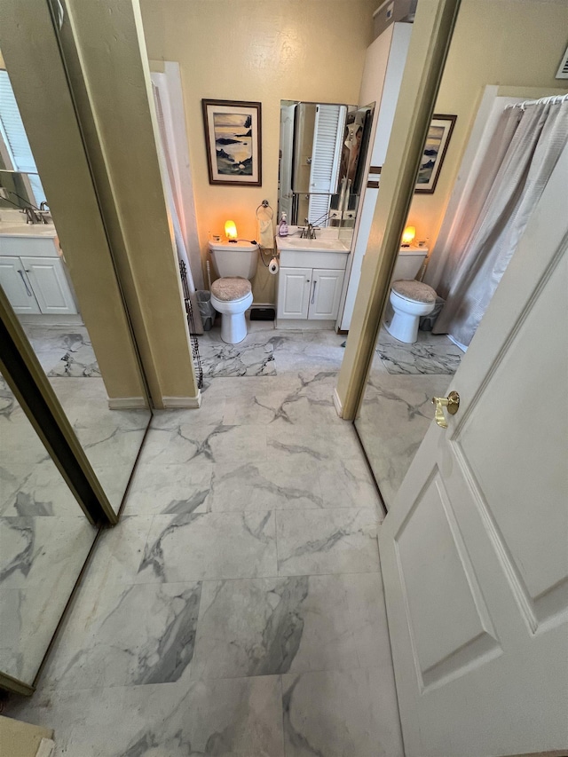 bathroom with marble finish floor, toilet, vanity, and baseboards