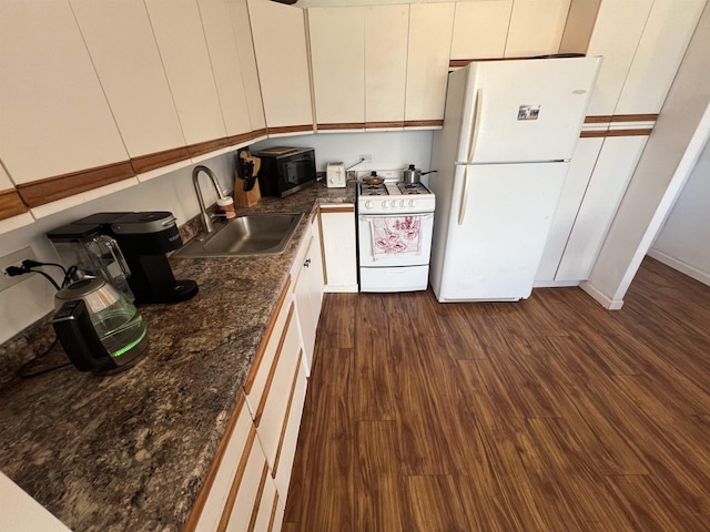 kitchen with white appliances, dark wood finished floors, a sink, white cabinetry, and dark countertops