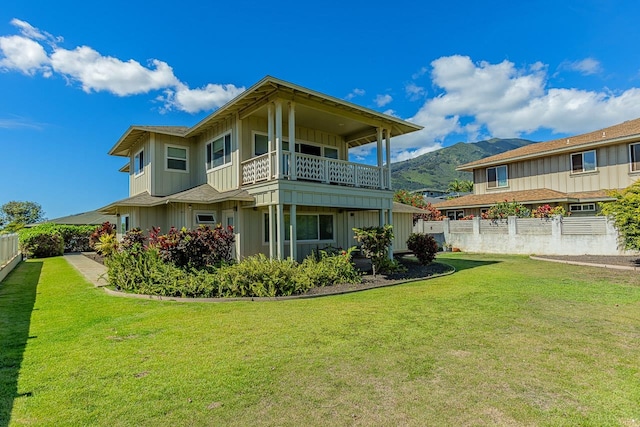 back of property with a balcony, a mountain view, and a lawn