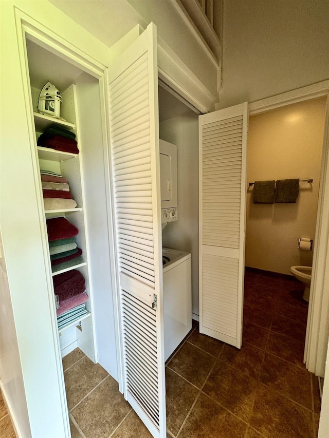 clothes washing area featuring dark tile patterned floors and stacked washer and dryer