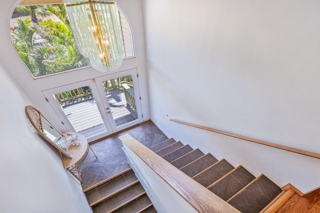 stairs with a towering ceiling, french doors, and a notable chandelier