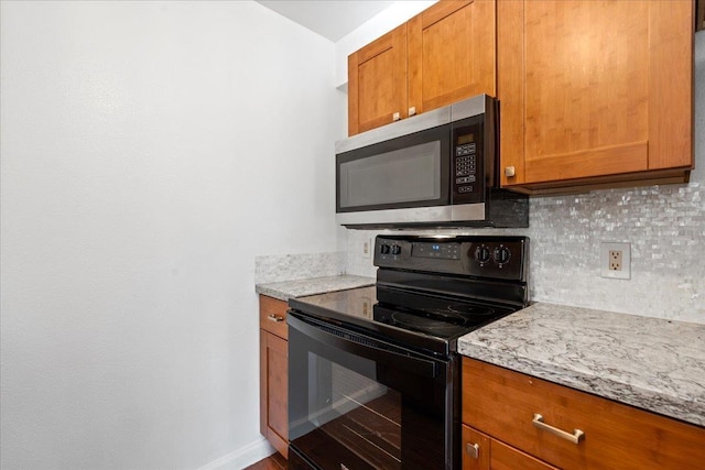 kitchen with tasteful backsplash, baseboards, brown cabinetry, stainless steel microwave, and black / electric stove