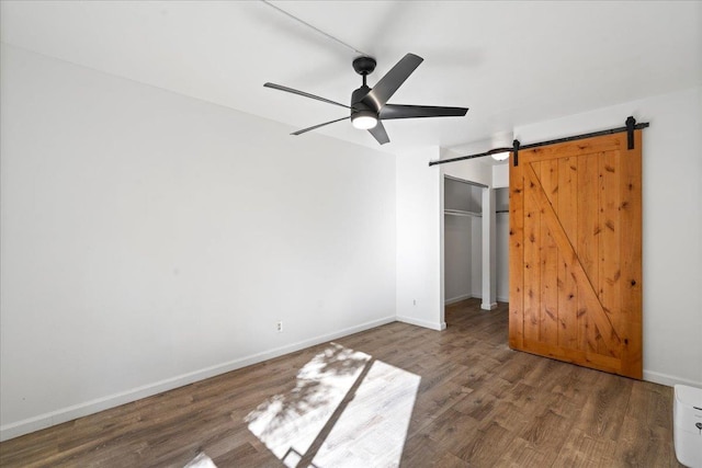 unfurnished bedroom featuring a barn door, wood finished floors, a ceiling fan, baseboards, and a closet