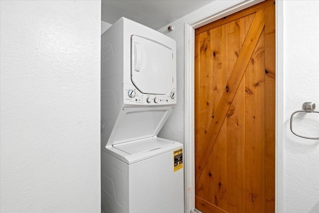 clothes washing area featuring laundry area, stacked washer / drying machine, and a textured wall