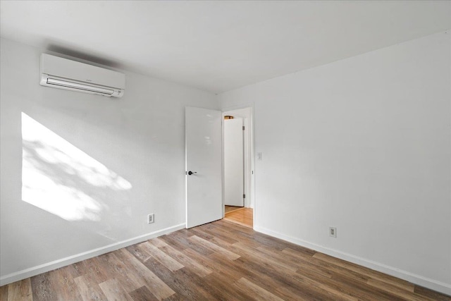 empty room with a wall mounted AC, wood finished floors, and baseboards