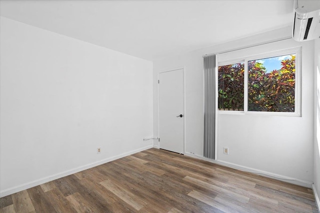 unfurnished room featuring baseboards, wood finished floors, and a wall mounted air conditioner