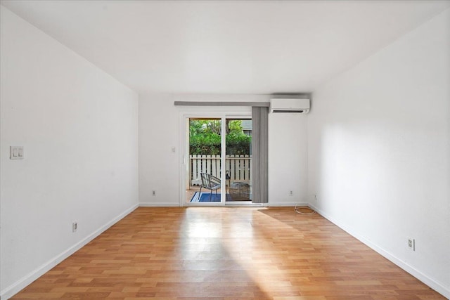 spare room with light wood finished floors, a wall mounted air conditioner, and baseboards