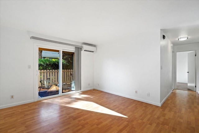 empty room with an AC wall unit, baseboards, and light wood finished floors