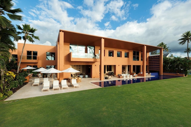 rear view of property featuring an outdoor pool, a lawn, a balcony, a patio area, and stucco siding