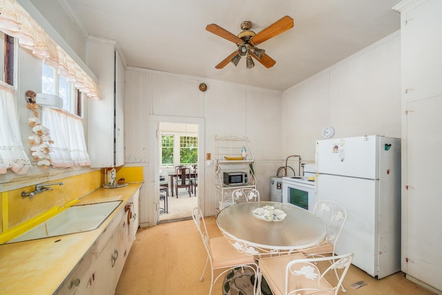 kitchen featuring a sink, white appliances, light countertops, a ceiling fan, and ornamental molding