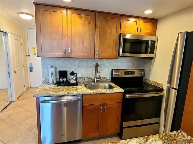 kitchen with sink, light tile patterned floors, stainless steel appliances, light stone counters, and decorative backsplash