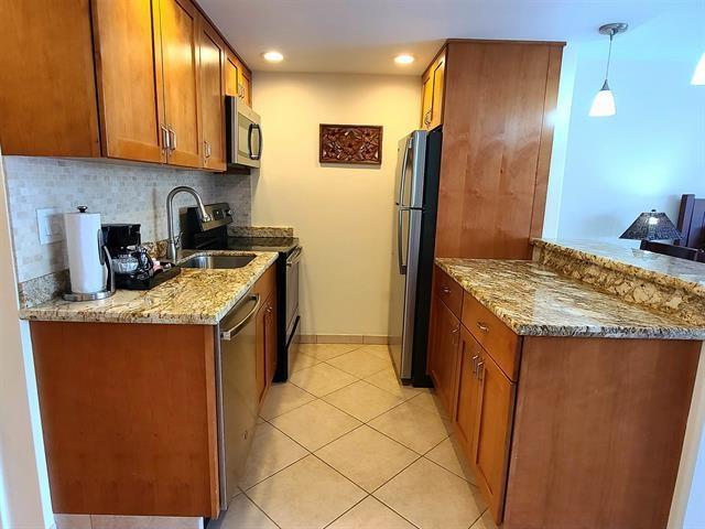 kitchen featuring sink, appliances with stainless steel finishes, hanging light fixtures, light stone counters, and decorative backsplash