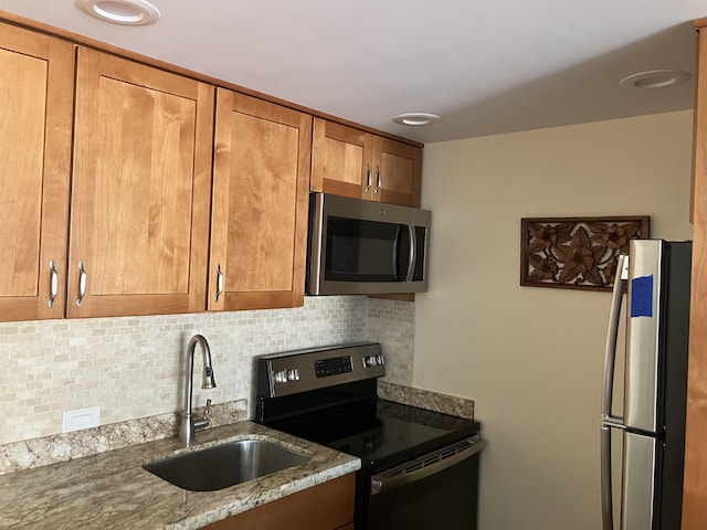 kitchen featuring appliances with stainless steel finishes, light stone countertops, sink, and backsplash