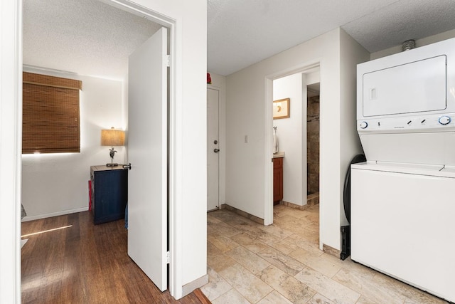 clothes washing area featuring a textured ceiling, light hardwood / wood-style flooring, and stacked washer / dryer