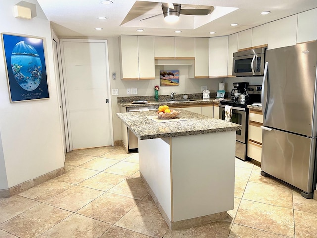 kitchen with light stone countertops, ceiling fan, stainless steel appliances, a kitchen island, and white cabinets