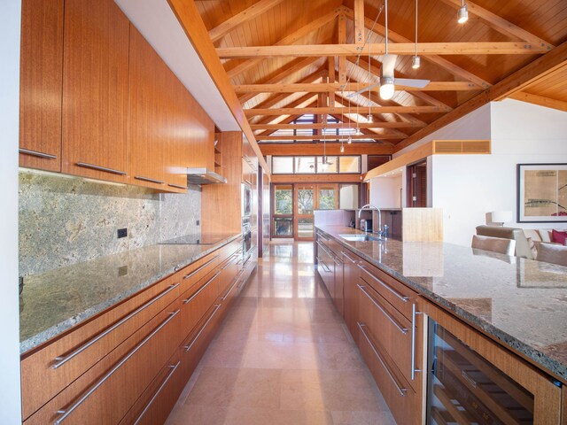 kitchen with hanging light fixtures, sink, dark stone countertops, beam ceiling, and beverage cooler