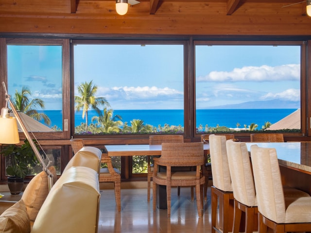 dining space with beam ceiling, a water view, and a wealth of natural light