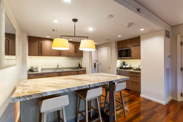 kitchen with a breakfast bar, sink, hanging light fixtures, dark hardwood / wood-style floors, and black microwave