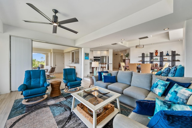 living room featuring light wood-type flooring, ceiling fan, and a raised ceiling