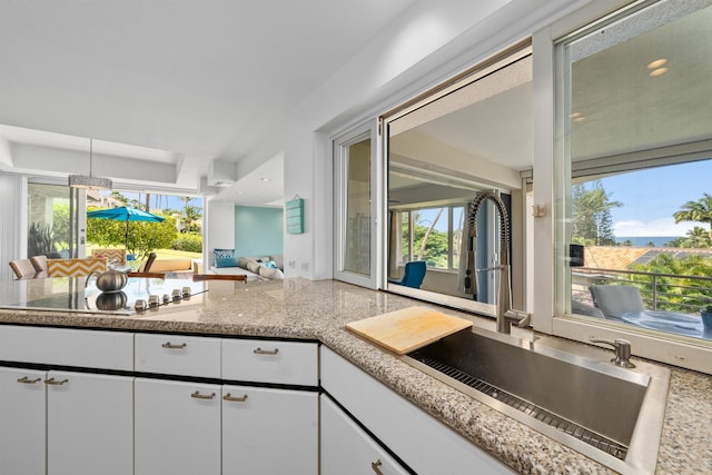 kitchen featuring stainless steel cooktop, white cabinetry, and sink