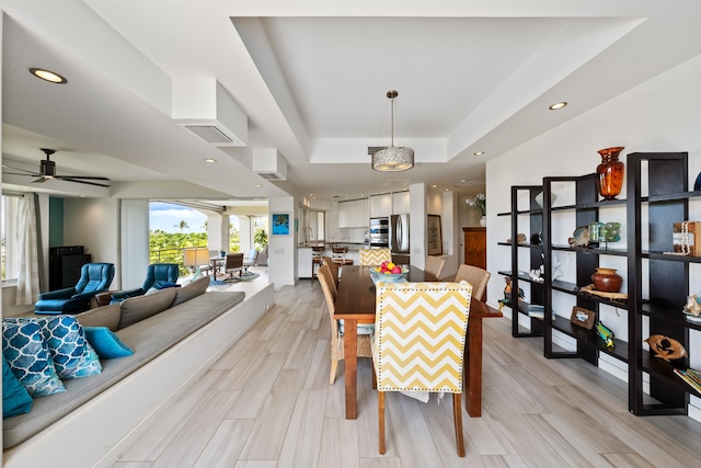 dining space with ceiling fan, a tray ceiling, and light hardwood / wood-style flooring