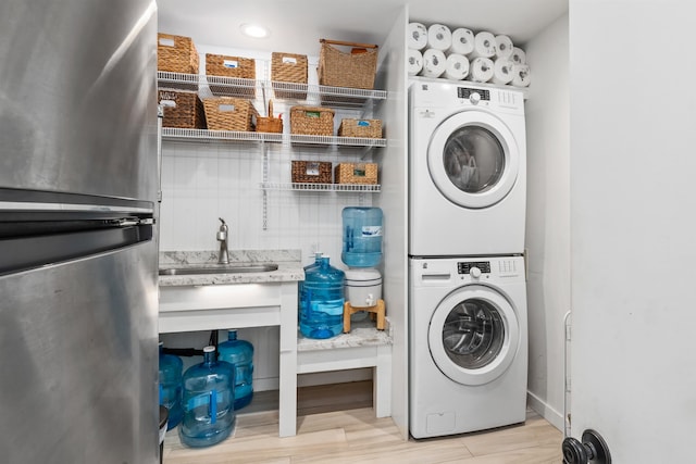 clothes washing area featuring sink, light wood-type flooring, and stacked washer and dryer