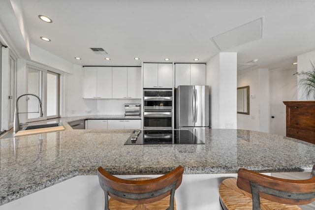 kitchen featuring sink, light stone counters, stainless steel appliances, kitchen peninsula, and white cabinetry