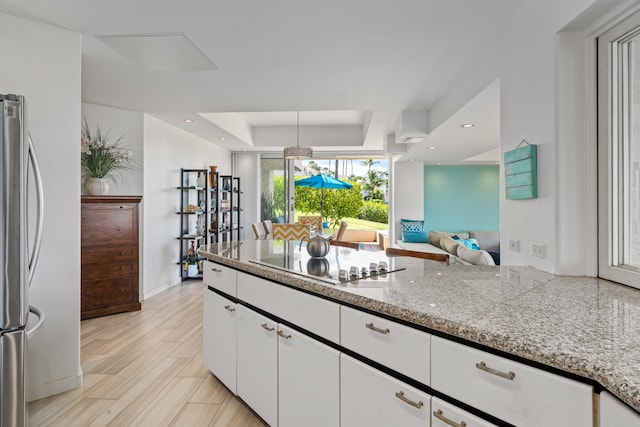 kitchen with black electric cooktop, stainless steel refrigerator, white cabinetry, and light hardwood / wood-style floors