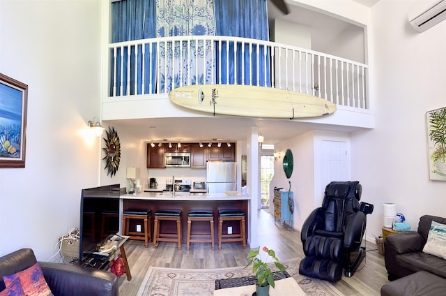 living room with a towering ceiling, a wall mounted AC, and light hardwood / wood-style flooring