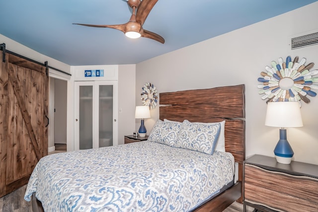 bedroom with ceiling fan, hardwood / wood-style floors, a closet, and a barn door