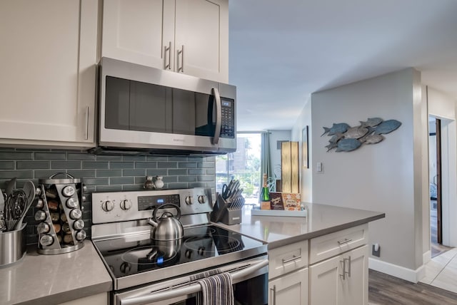 kitchen featuring backsplash, white cabinetry, appliances with stainless steel finishes, and hardwood / wood-style flooring