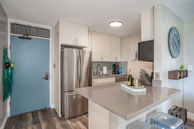 kitchen with white cabinetry, a kitchen breakfast bar, sink, kitchen peninsula, and stainless steel refrigerator