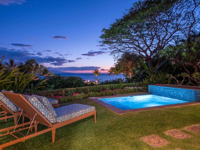 pool at dusk featuring a water view and a yard