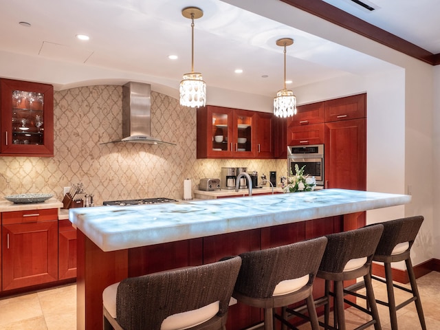 kitchen with pendant lighting, a kitchen island, an inviting chandelier, appliances with stainless steel finishes, and wall chimney range hood