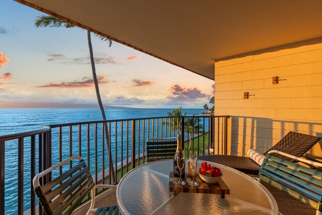 balcony at dusk featuring a water view