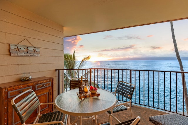 balcony at dusk featuring a water view