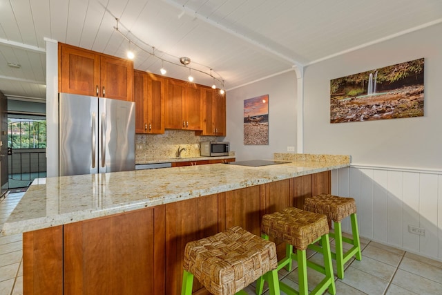 kitchen with light tile patterned floors, stainless steel appliances, kitchen peninsula, and light stone countertops