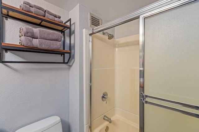 full bathroom with bath / shower combo with glass door, visible vents, toilet, and a textured wall