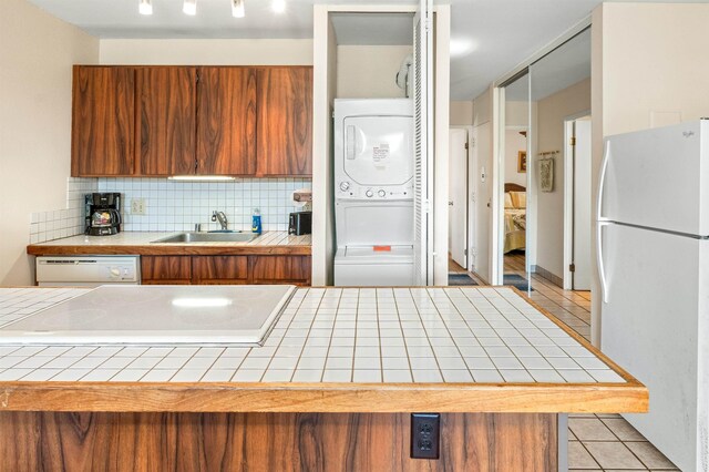 kitchen featuring white appliances, light tile patterned floors, tile counters, sink, and stacked washing maching and dryer