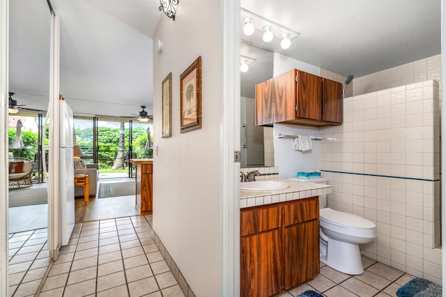 bathroom featuring toilet, tile patterned flooring, vanity, ceiling fan, and tile walls