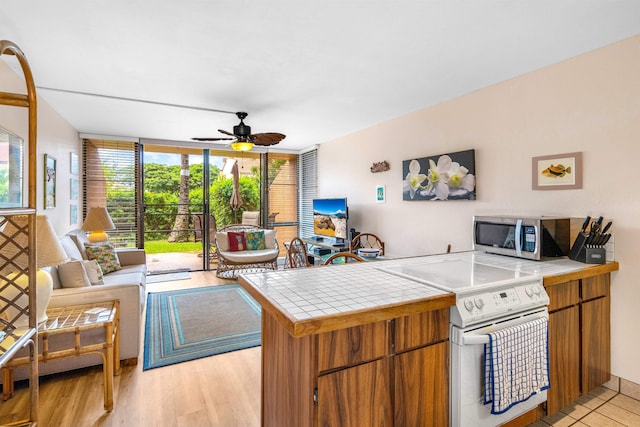 kitchen featuring light wood-type flooring, tile counters, white electric stove, kitchen peninsula, and ceiling fan