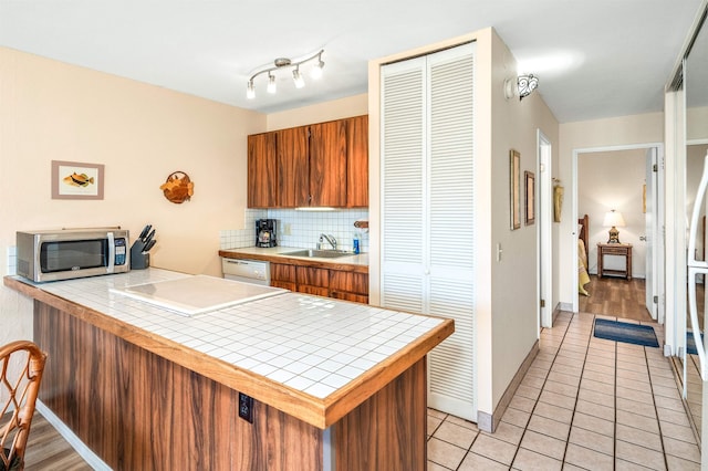 kitchen featuring tile countertops, tasteful backsplash, kitchen peninsula, sink, and light wood-type flooring