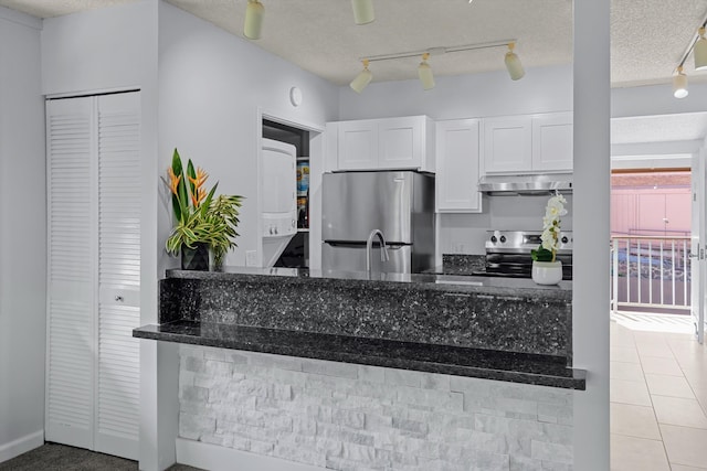 kitchen featuring white cabinets, range hood, stacked washer and dryer, and appliances with stainless steel finishes