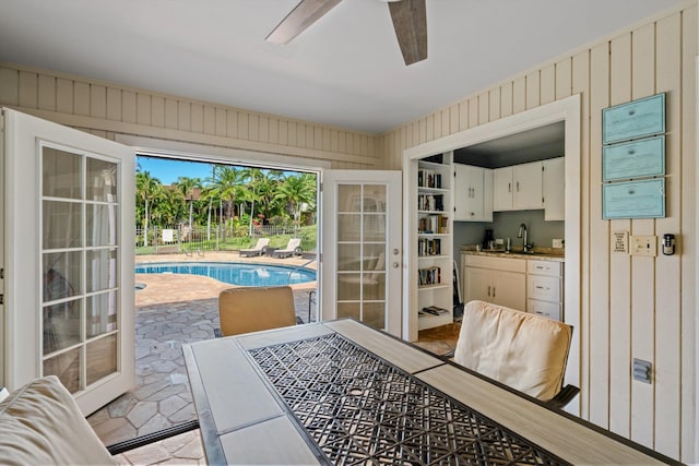 doorway to outside featuring ceiling fan, wooden walls, and sink