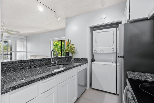 kitchen with sink, stacked washing maching and dryer, a textured ceiling, appliances with stainless steel finishes, and white cabinetry