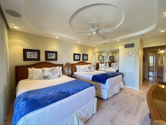 bedroom with a raised ceiling, ceiling fan, a closet, and light carpet