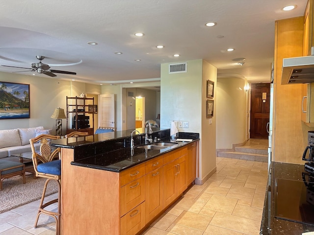 kitchen featuring dark stone counters, a kitchen bar, sink, ceiling fan, and ventilation hood