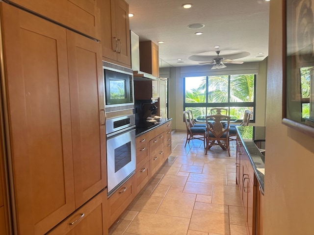 kitchen featuring ceiling fan, wall chimney exhaust hood, and stainless steel oven