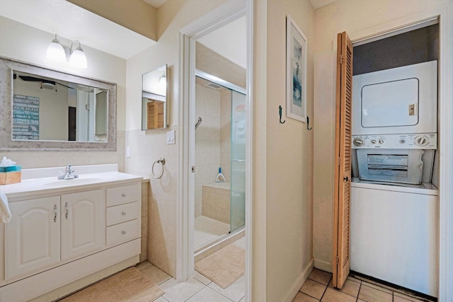 bathroom featuring tile patterned flooring, vanity, stacked washer / drying machine, and an enclosed shower